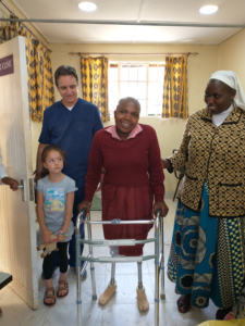 Steve and Remi standing with young woman who is walking for the first time on two new legs. A Sister is to her right.